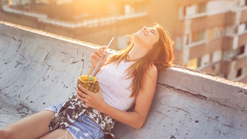 Frau genießt Drink aus einer Ananas und sonnt sich liegend Auszeit vom Alltag nehmen